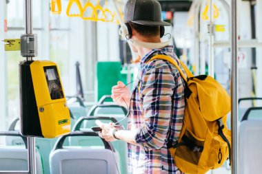 Genç aman kafasında kulaklık ile bir otobüste duruyor ve müzik dinliyor.