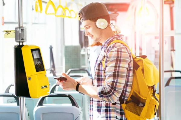 Joven hombre está de pie en un autobús con auriculares en la cabeza y escuchar la música . — Foto de Stock