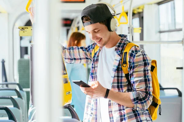 Joven está de pie en un autobús con auriculares en la cabeza y escuchando la música . — Foto de Stock