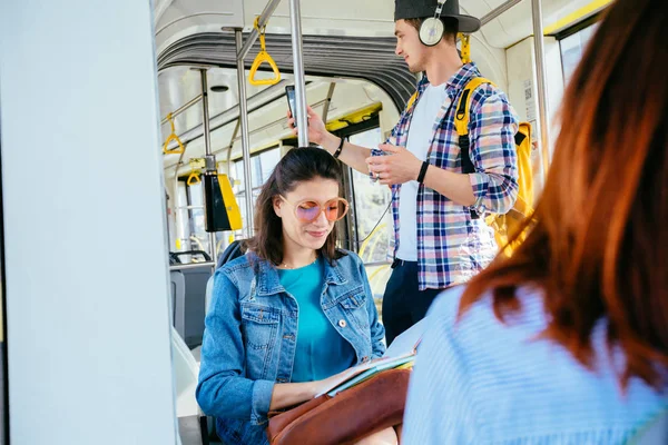 Joven mujer hermosa con gafas de sol en la cabeza se apoya contra la barra de autobús y se aferra a su bolsa de equipaje mientras viaja en autobús . — Foto de Stock