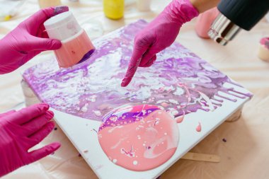 Kadın sanat terapisi sınıfında sıvı akrilik soyut resim oluşturma eğitimi, tuval üzerine boyalar bırakarak çalışırken kadın saç kurutma makinesi tutan kadın ressam. Takım çalışması, çalışma, sanat terapisi konsepti.