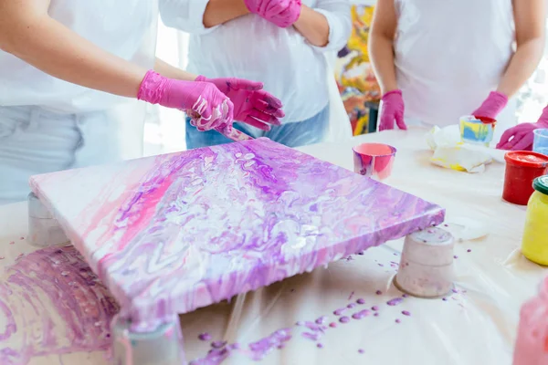 Vrouw schilder houdt haardroger terwijl vrouwelijke beginnres studeren het creëren van vloeistof acryl abstract schilderij in kunst therapie klasse, het laten vallen van verven op canvas. Teamwork, studie, kunst therapie concept. — Stockfoto