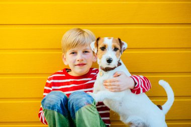 Sarı arka planda esneyen köpeği Jack Russell Terrier ile oynayan mutlu çocuk portresi. Arkadaşlık ilişkisi sadakat duygusu konsepti.