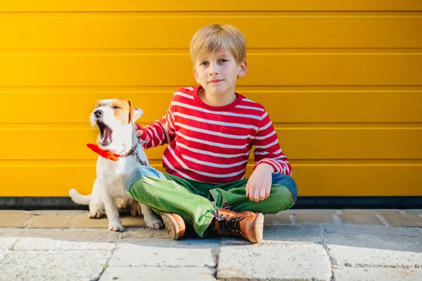 Portret van een gelukkige knappe jongen die hand in hand speelt met zijn hond Jack Russell Terrier op gele achtergrond buiten. Vriendschapsgevoel concept. — Stockfoto