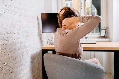 Arka taraftaki manzarayı kapat. Yorgun, serbest çalışan kadın başını tutarken boynuna masaj yapıyor. Pasif yaşam tarzı, yanlış duruş, boyun ve sırt ağrısı konsepti.