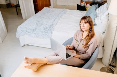 Dizüstü bilgisayar kullanırken kameraya bakan kadın serbest yazar. O, ev içi masada oturuyor. Ev kavramından çalışmak.