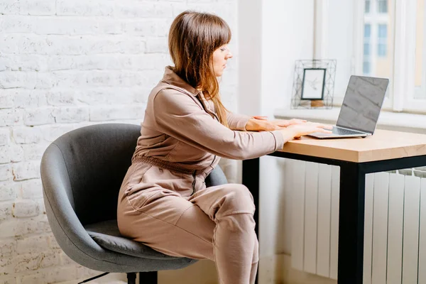 The correct position posture when working at the computer. A woman sits at a table with a laptop computer. Spinal curvature. Good posture. Healthy back.