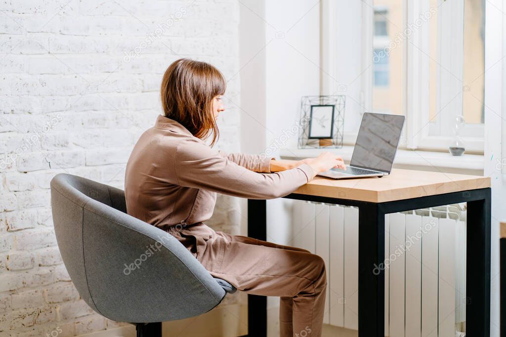 The correct position posture when working at the computer. A woman sits at a table with a laptop computer. Spinal curvature. Good posture. Healthy back.