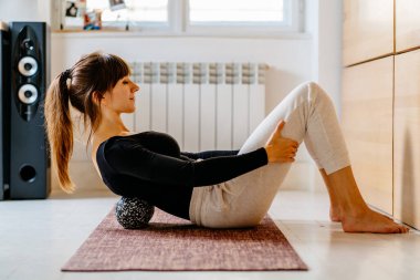 Spor giyimli bir kadının evde ya da ofiste yoga minderinde uzanan omurga egzersizi için duoball kullanması acının ve rehabilitasyon konseptinin üstesinden gelmesi..