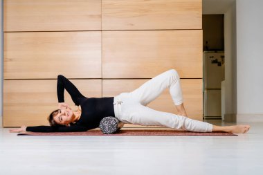 Esmer kadın yoga pilates eğitmeni, siyah gömlekli, beyaz pantolonlu, masaj için köpük silindirli egzersiz yapıyor. yoga ve sağlıklı yaşam tarzı teması.