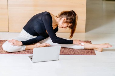 Fitness sanal sanal egzersiz konsepti. Kadın eğitmen evde internetten yayın yapıyor. Spor giyim işindeki sporcu kız spor yapıyor. Oturma odasında egzersiz, dizüstü bilgisayar ve köpük silindiri..