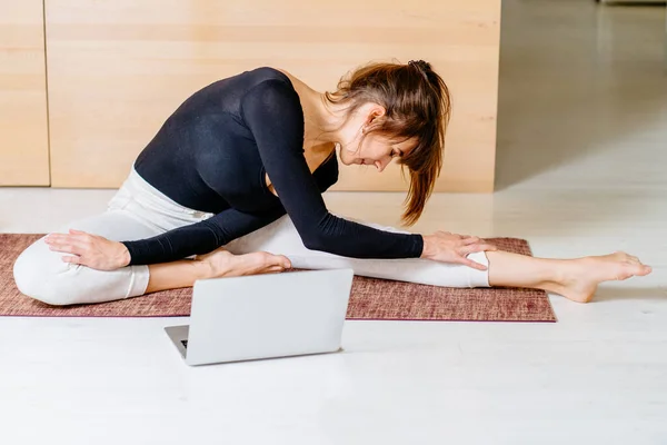 Fitness virtual online exercise concept. Woman instructor streaming from internet at home. Sporty girl in sportswear working out. Workout training in living room, laptop and foam roller a side.