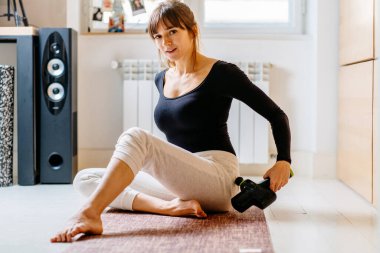 Genç ve çekici bir kadının kalçaları için masaj tekniği uyguladığı, evde ya da stüdyoda pilates minderinde otururken çekilmiş hayat tarzı bir fotoğraf..
