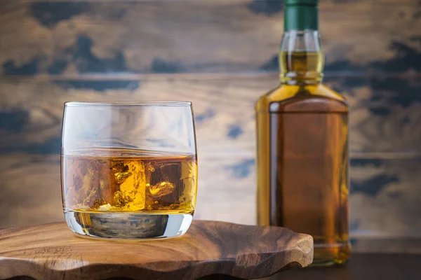 バーボンやスコッチボトルで木製のテーブルの上に氷のキューブを獲得ゴールデンウイスキー アルコール飲料 — ストック写真