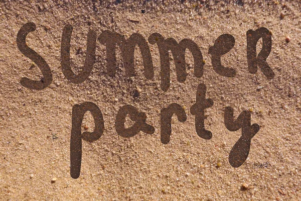 Summer party text hand drawn on a beach sand