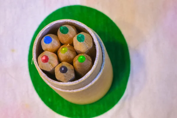 Colored pencils inserted in a cardboard cylinder on a colored plane, horizontal image