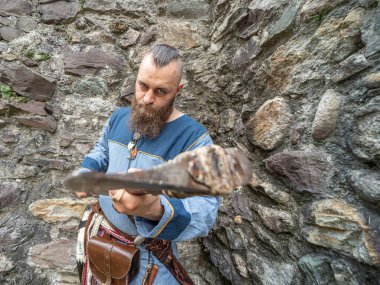 Taş bir duvarın önünde balta sallayan genç bir Viking portresi.