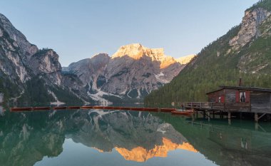 Arayıcı dağları ve ahşap tekneler sabahın ilk ışıklarıyla Braies Gölü 'nün sularına yansıdı. Pragser Wildsee' de Prag Gölü olarak da bilinir. Güney Tyrol 'daki İtalyan Dolomitleri' nde bir kulübe ve dağ manzarası da görülebilir.