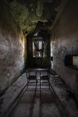 Terk edilmiş ve çökmüş bir akıl hastanesinin dar bir sınıfındaki okul masası.