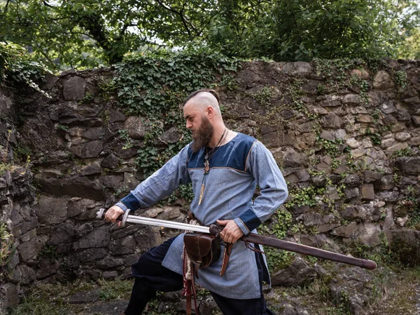 中世の戦士は鞘から剣を引き 伝統的な衣服でバイキングを描く — ストック写真