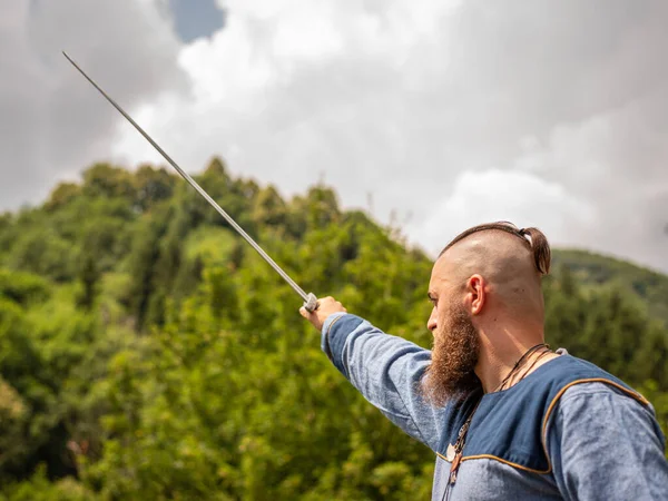 Ortaçağ savaşçısı kılıcını savurup gökyüzüne kaldırıyor. Geleneksel kıyafetlerle Viking.