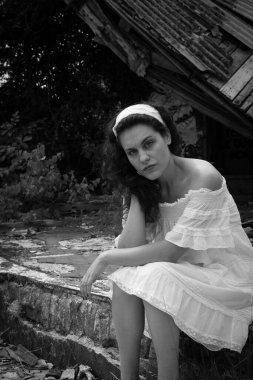 Açık renk elbiseli güzel bir kadın hayalet bir kasabanın yıkıntılarının önünde oturuyor.