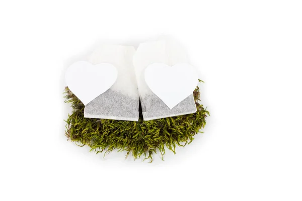 Close-up of two tea bags with white heart tag on peace of grass