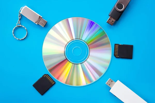 Glowing DVD with rainbow colors on a blue board with usb flash drives and cards - flatlay photography