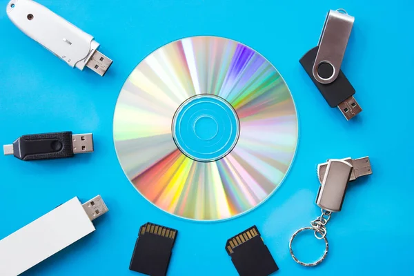 Glowing DVD with rainbow colors on a blue board with usb flash drives and cards - flatlay photography