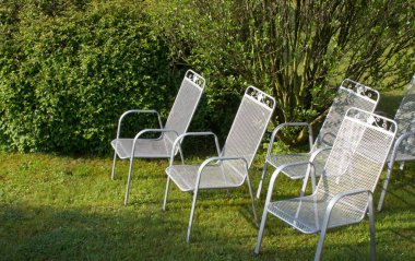 Metalik Gümüş Sandalye Park çimenlerin üzerinde. Arka planda çalılar vardır.