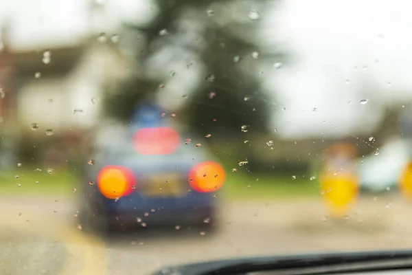 rain drops on the window of a car and smudged cars and people and pedestrians. raindrops in focus and blurred background.