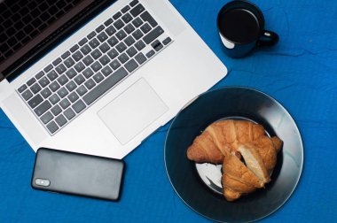 Tipik blogger sabah. Dizüstü bilgisayar ve akıllı telefon yatakta. Lezzetli kahve ile Kruvasan