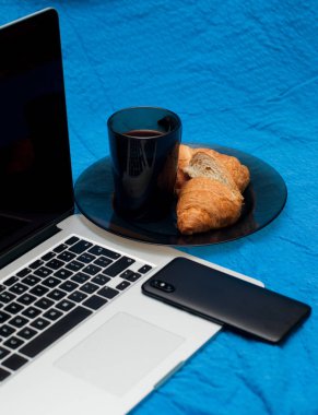 Tipik blogger sabah. Dizüstü bilgisayar ve akıllı telefon yatakta. Lezzetli kahve ile Kruvasan