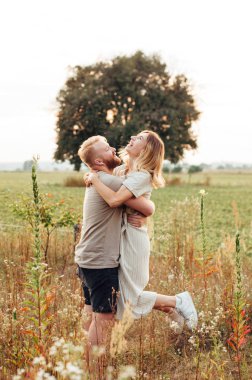 Yakışıklı adam ve sarışın kız güzel bir sıcak gün batımında alanında yürüyor. yavaşça sarılmak, güneşte ayakta