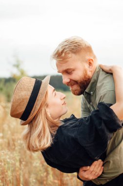 Yakışıklı adam ve sarışın kız güzel bir sıcak gün batımında alanında yürüyor. yavaşça sarılmak, güneşte ayakta