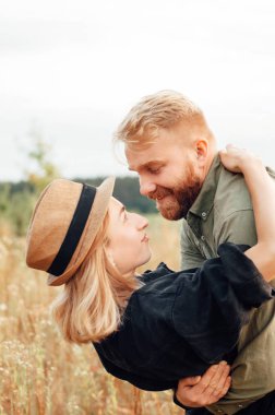 Yakışıklı adam ve sarışın kız güzel bir sıcak gün batımında alanında yürüyor. yavaşça sarılmak, güneşte ayakta