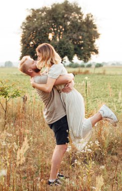 Yakışıklı adam ve sarışın kız güzel bir sıcak gün batımında alanında yürüyor. yavaşça sarılmak, güneşte ayakta