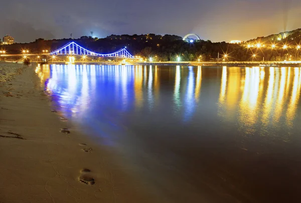 Reflection of the lights of night Kyiv and traces of barefooted on the sand of the embankment of the Dniro River
