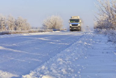 Sabahın erken saatlerinde, gümüş ile kaplı bir çalı boyunca karla kaplı beyaz yol boyunca ağır kamyon konvoyu rides.