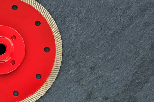 Half of the diamond cutting wheel is red with a threaded nut, on the right side is a copy space on a gray granite background close-up.