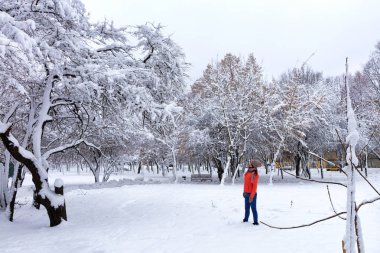 Genç güzel kadın parlak bir mercan ceket ve kot karla kaplı masal Park Ahşap banklar ile kış giriyor