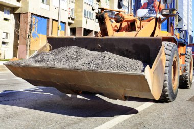 Ağır inşaat buldozer eski yıpranmış asfalt bir yolda bir şehir öğlen sokak inşaatı sırasında bir kepçe taşır