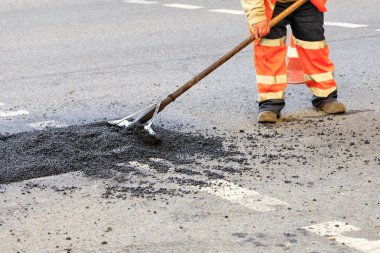 A road builder collects fresh asphalt on part of the road and levels it for repair in road construction. clipart