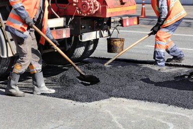 The working team renews a portion of asphalt with shovels in road construction clipart
