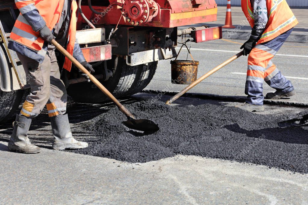 The road workers' working group renews a part of the road with fresh asphalt and levels it for repair in road construction.