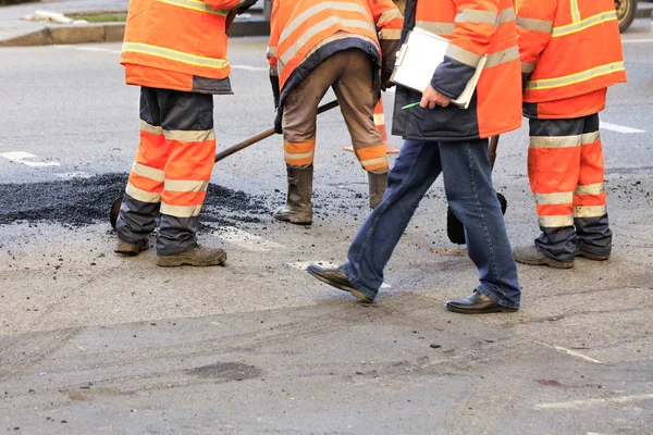 Un equipo de constructores de carreteras recoge y alinea asfalto fresco con una pala a lo largo de la parte reparada de la carretera . — Foto de Stock
