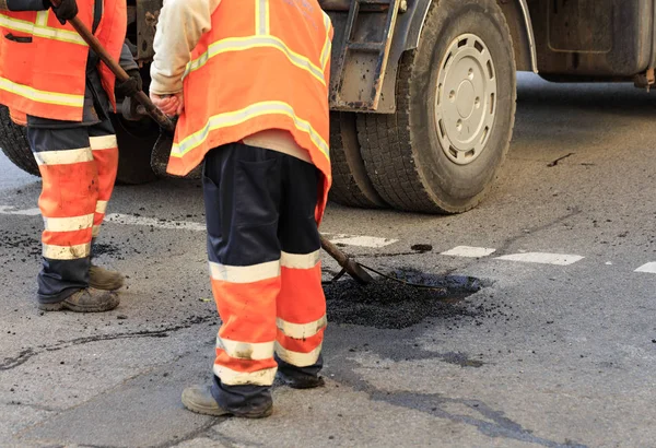 Two road builders assemble and level fresh asphalt with a shovel and level on the repaired part of the road.