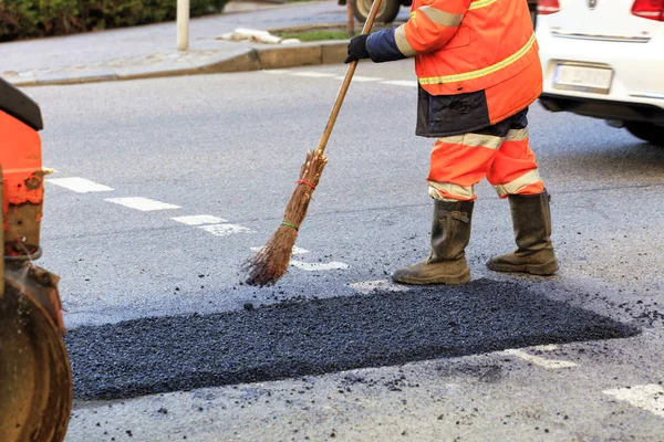 Un constructor de carreteras recoge asfalto fresco en parte de la carretera y lo nivela para su reparación en la construcción de carreteras . — Foto de Stock