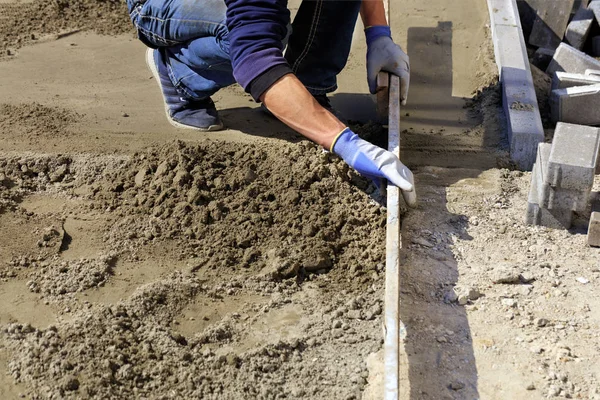 Trabajador alinea los cimientos con una plancha de madera para colocar baldosas en la acera . — Foto de Stock