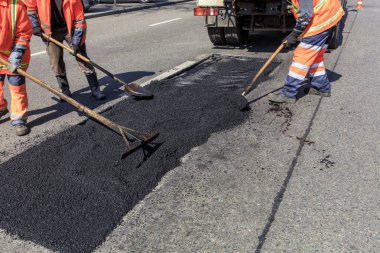 Çalışma ekibi, asfalt parçasını yol inşaatı sırasında küreklerle eşit şekilde dağıtır..